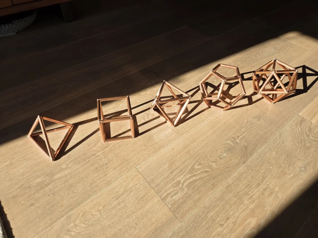 De vijf handgemaakte koperen platonische lichamen van Being in Harmony op een rij